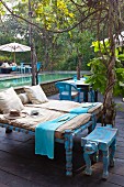 Sun loungers with cushions and animal-shaped stool on terrace in front of large pool of water in tropical garden