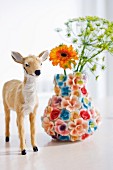Small deer figurine next to vase covered with ceramic flowers