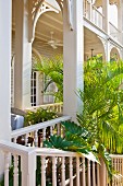 Elegant veranda with rounded arches attached to elegant, white, colonial-style building with palm trees