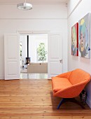 Orange sofa on wooden floor in foyer with open double doors and view into living room beyond