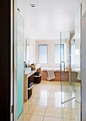 View into bathroom with beige floor tiles; laundry baskets below stone washstand and half-opened shower door