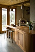 Curved, wooden kitchen counter and dainty bar stools in front of terrace doors with a view of the garden