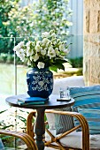 Bouquet of white flowers in blue china vase on round side table in front of glass balustrade