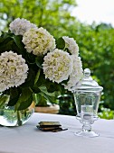 Outside: bouquet of hydrangeas and chalice shaped outdoor glass candle holder on a table set in white