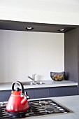 Red kettle on gas hob on island counter in front of modern, grey kitchen counter