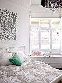 Weisses Doppelbett mit grünem Kissen und romantischem Wandprint; Fensternische mit gemütlicher Sitzbank
