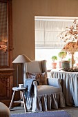 Rustic wooden stool with integrated reading lamp next to wing-back chair with romantic valance