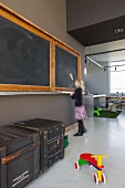 Open-plan interior with old blackboard in converted school building; old transport crates and colourful wooden scooter on polished concrete floor