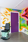 Corner of room with graffito mural and vintage dentist's chair on concrete floor