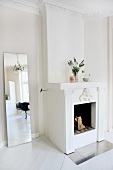 White out - modern full-length mirror next to open fireplace in renovated interior with stucco frieze