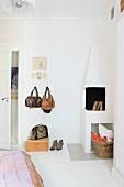 Handbags hanging on wall hooks next to open corner fireplace in bedroom