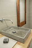 Concrete sink on wooden counter and designer wall-mounted tap fitting next to mirror with antique wooden frame