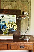 Retro table lamp with chrome base next to posy on simple console table in front of architectural picture