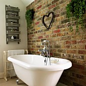 Free-standing, vintage bathtub against brick wall with planters and ornamental heart