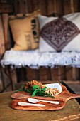 Chanterelles, walnuts, herbs and wooden spoons on wooden board; cushions on wire bench in blurred background