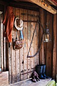 Leather jacket and ladies' hat hanging on board door of woodshed next to hacksaw and lantern