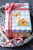 Gift box festively decorated with gingerbread stickers, red and white checked ribbon and candy canes