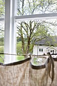 Vorhang auf gespanntem Seil vor Sprossenfenster und Blick in den Garten auf traditionelles Landhaus