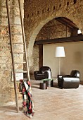 Armchairs with black leather upholstery on terracotta tiles in spacious, restored stone house