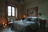 Double bed with modern, stone grey bedspread contrasting with wood-panelled headboard, small items of antique furniture and Rococo-style sconce lamps