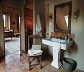Vintage-style bathroom with old terracotta tiles and crystal sconce lamps above French pedestal washbasin