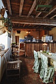 Stilistische Gegensätze in rustikaler Wohnküche - mit edlen Stoffen drapierter Essplatz unter grober Holzdecke