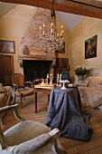 Chandelier with lit candles in rustic living room with traditional seating and brocade tablecloth draped on simple wooden table