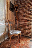 Upholstered chair with Rococo-style gilt wooden frame and processional staff leaning on brick wall in corner of room