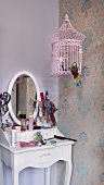 Romantic girls' dressing table and pink bird cage against wallpaper with traditional pattern