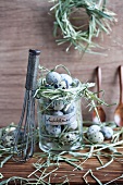 Whisk leaning on jar filled with quails' eggs and wreathed in hay