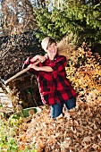 Woman standing in heap of autumn leaves with besom broom on shoulder