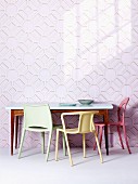 Verschiedenfarbige Kunststoff Stühle vor Tisch im Fiftiesstil an Wand mit dreidimensionalem Muster auf Tapete