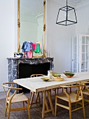 Klassiker Holzstühle an schlichtem Esstisch aus Holz vor Kamin mit Steinschürze unter hohem Spiegel mit Goldrahmen