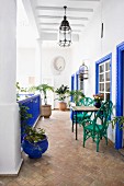 Green chairs between window frames and balustrade painted bright blue on veranda of Moroccan courtyard