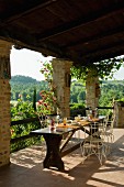 Gedeckter Tisch und filigrane Metall Stühle auf überdachter Terrasse mit Blick in die toskanische Landschaft