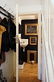 Coat rack in foyer and view of gilt picture frames on black wall and corner sink through open door