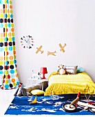 Aufgeklebte Flugzeuge, bunte Wanduhr und Retro-Vorhang mit farbigen Kreisen hinter Kinderbett