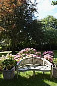 Geschwungene Gartenbank vor blühenden Hortensienbüschen