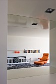 Minimalist bedroom with niche used as bookcase and orange designer armchair