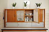 Potted house plants on 50s kitchen dresser with open door showing white crockery inside