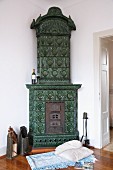 Blanket and cushions on wooden floor in front of green-tiled corner stove with vintage hearth equipment