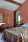 Doppelbett mit bunter, karierter Tagesdecke in rosa getöntem Schlafzimmer unter dem Dach