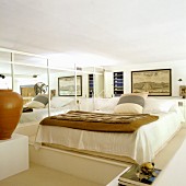 Bedroom decorated in natural shades with double bed on platform next to mirrored wall