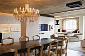 Long dining table and vintage chairs below chandelier in loft-style interior with exposed concrete ceiling