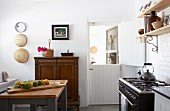 Bright, vintage-style kitchen with retro gas cooker and simple wooden shelving on white-tiled wall
