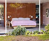 Blick auf Schlafbereich mit Beet in verglastem Wohnhaus