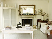 Living room with open fireplace, wall mirror, white-painted table, armchairs, corner cupboard and antique side table