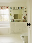Helles Badezimmer mit weissen Möbeln, Wandspiegel mit Wimpelkette und weißem Holzboden
