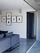 View from balcony of open, blue wooden door, living room couch in same colour and collection of pen and ink drawings on wall