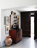 Entrance area with heavy, open front door and collection of statues and pictures; artistic terracotta vase on floor next to old, Chinese chest
